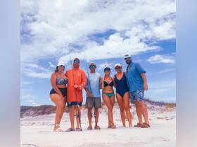 A cheerful group of friends poses on the beach, ready for a day of fishing under the sunny sky — perfect for creating unforgettable memories on the water.