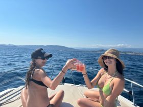 Two friends toast with cocktails on the deck of a boat under the sun, capturing the essence of a perfect day on the water.