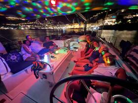 A lively group enjoys a night celebration aboard a boat, surrounded by colorful lights and a beautiful waterfront backdrop — perfect for unforgettable boat parties.