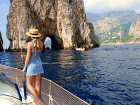 A woman enjoys the stunning coastal views while standing on the deck of a boat near iconic rock formations, perfect for exploring the beautiful landscapes of Capri.