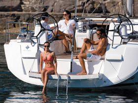 A group enjoys a sunny day on a yacht, with one person relaxing on the swim platform and others lounging on deck — perfect for summer adventures on the water.