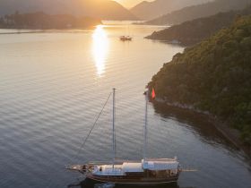 A stunning aerial view of a yacht anchored in serene waters at sunset, surrounded by lush hills — perfect for showcasing luxury boating experiences.
