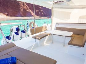 Interior view of a spacious lounge area on a boat, featuring comfortable seating and a table, perfect for relaxing while enjoying the scenic turquoise waters.
