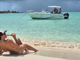 Guests relax on the beach with drinks while a boat is anchored nearby, capturing the essence of a perfect day on the water.