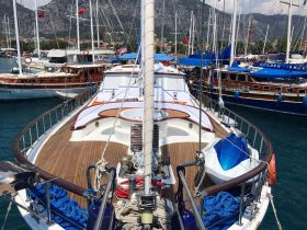 A stunning view of a yacht docked at a marina, showcasing its elegant design and wooden deck, surrounded by other boats against a picturesque mountainous backdrop.