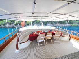 A beautifully set dining area on a yacht, featuring a round table adorned with food and drinks, perfect for enjoying meals while surrounded by stunning coastal views.