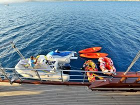 A variety of water toys including a jet ski, kayaks, and inflatable tubes are ready for fun on the water, with a person preparing to use the equipment.