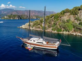 A stunning aerial view of a beautifully crafted yacht docked in serene waters, surrounded by lush greenery and rocky landscapes — perfect for luxury sailing experiences.
