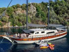 A group of crew members stands proudly on the deck of a luxurious yacht, showcasing the vessel's elegance against a stunning natural backdrop — perfect for charter experiences.