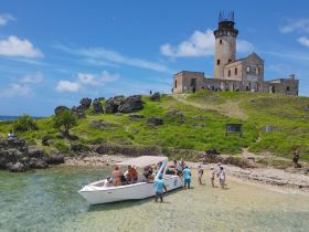 A lively group of guests disembarks from a boat at a scenic beach near a historic lighthouse, perfect for exploration and adventure.