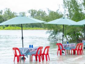 Colorful outdoor dining setup with tables and umbrellas in shallow water, perfect for enjoying meals by the beach.