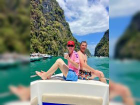 A couple enjoys a sunny day on a boat, sipping drinks and taking in the stunning scenery of lush cliffs and turquoise waters — perfect for a memorable adventure.