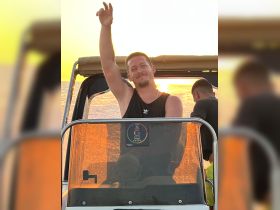 A joyful moment captured at sunset with a man waving from the helm of a boat, embodying the spirit of celebration on the water.