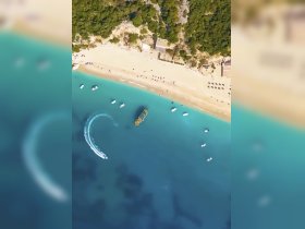 Aerial view of a vibrant beach scene with various boats anchored in turquoise waters, showcasing a perfect day for water sports and relaxation.