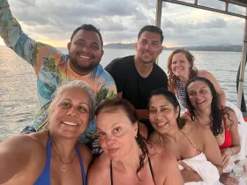 A joyful group of friends poses for a selfie on a boat, capturing the essence of their fun-filled day on the water as the sun sets in the background.