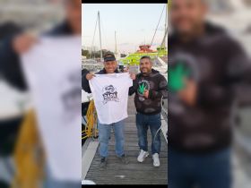 Two friends celebrate their fishing tour with a commemorative shirt at the marina, showcasing the excitement of their adventure.