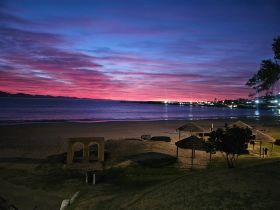 A stunning sunset paints the sky in vibrant hues over a serene beach, creating a picturesque coastal scene perfect for evening strolls or romantic getaways.