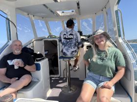A cozy interior shot of a boat featuring two guests relaxing in the cabin, showcasing the helm area and comfortable seating — perfect for enjoying a day on the water.
