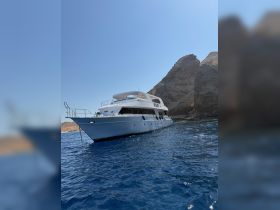 A stunning yacht anchored near rocky cliffs, showcasing its elegant design against a clear blue sky and tranquil waters — perfect for luxury charters and scenic tours.