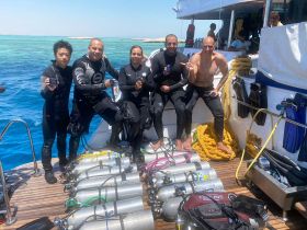 A group of divers celebrates their adventure on a boat, showcasing their scuba gear and excitement for the underwater exploration ahead.