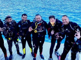 A group of divers poses happily before their underwater adventure, showcasing the excitement of scuba diving in crystal-clear waters.