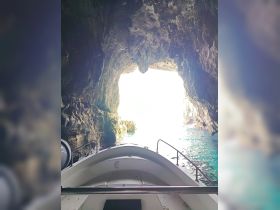 A scenic view from the bow of a boat entering a stunning cave, showcasing the natural beauty of the surrounding rock formations and the bright light at the cave's exit.