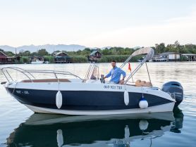 A man poses on a sleek boat at the dock, showcasing the serene waters and surrounding nature — perfect for leisurely outings or fishing trips.