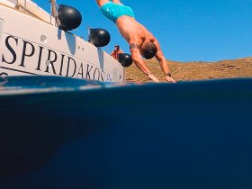 A man dives off the side of a boat into crystal-clear waters, capturing the thrill of summer adventures on the water.