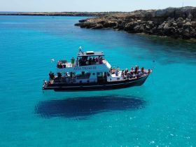 A lively group enjoys a cruise aboard the AYIA TRIAS III, surrounded by stunning turquoise waters — perfect for exploring coastal beauty.