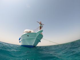 A woman stands triumphantly on the bow of a boat, enjoying the ocean breeze — a perfect moment of adventure on the water.