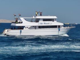 A lively yacht named 'Abe Mesad' cruises through the vibrant waters, with guests celebrating on deck — perfect for unforgettable adventures on the sea.
