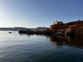 A serene view of a rocky coastline with calm waters and a distant harbor, perfect for capturing the beauty of nature and coastal landscapes.