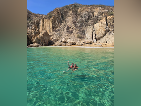 Two friends enjoy a refreshing swim in crystal-clear waters, surrounded by stunning rocky cliffs — a perfect moment of fun and relaxation on the beach.