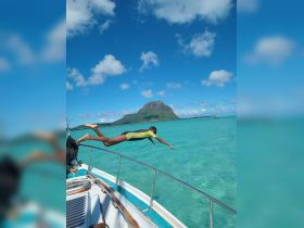 A child joyfully leaps off the side of a boat into the crystal-clear waters, with a stunning island backdrop — a perfect moment of fun and adventure on the water.