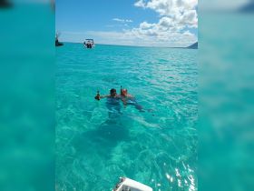 Two friends enjoy a refreshing swim in crystal-clear waters, celebrating with drinks in hand — a perfect moment for relaxation and fun in the sun.