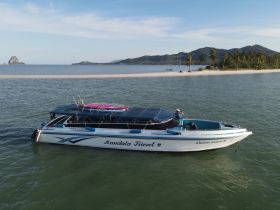 Aerial view of a sleek speedboat named 'Kandala Travel 2' docked in calm waters, surrounded by a picturesque landscape of islands and sandy beaches — ideal for exploring tropical destinations.