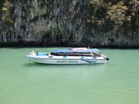 A sleek speedboat named 'Mandala Travel' is docked in tranquil green waters, surrounded by stunning rock formations, perfect for exploring scenic destinations.