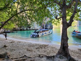 A child fishes on the sandy beach while boats are anchored in the serene turquoise waters, showcasing a picturesque tropical scene.
