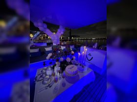 An elegantly set table featuring a cake, cocktails, and floral decorations aboard a boat, perfect for celebrations or special events under the night sky.