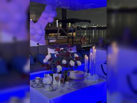 An elegantly set table on a boat featuring a cake, champagne flutes, and floral arrangements, perfect for celebrations or special events on the water.