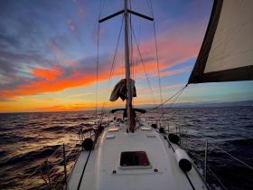 A stunning sunset view from the deck of a sailboat, showcasing the vibrant colors of the sky as the vessel sails through the open water.
