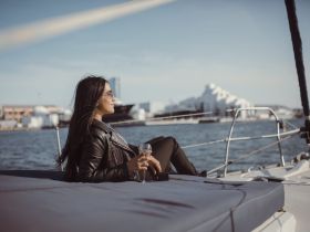 A woman enjoys a cocktail while relaxing on the deck of a sailboat, capturing the essence of leisure and elegance on the water.