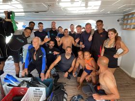A lively group of divers poses for a photo on board, showcasing excitement for their upcoming underwater adventure — perfect for family and friends looking to explore the ocean together.