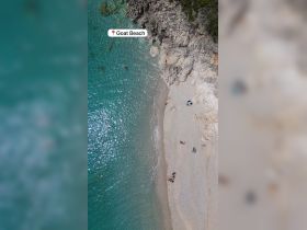 Aerial view of Goat Beach showcasing its stunning turquoise waters and sandy shore, with visitors enjoying the sun and swimming — a perfect destination for relaxation and fun.