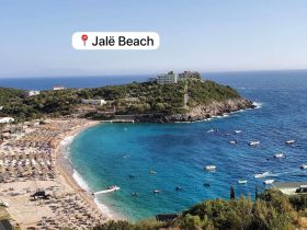 A stunning aerial view of Jalë Beach, showcasing the vibrant coastline, sunbathers, and boats dotting the turquoise waters — a perfect destination for beach lovers and water activities.