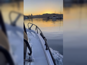 A serene view of a boat navigating through calm waters at sunset, with a picturesque backdrop of a harbor and distant buildings, perfect for showcasing tranquil boating experiences.