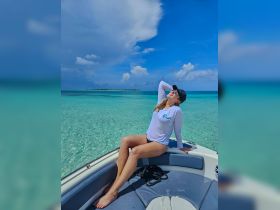 A woman enjoys the sun while relaxing on the bow of a boat, surrounded by stunning turquoise waters — a perfect moment for beach lovers and boat enthusiasts.