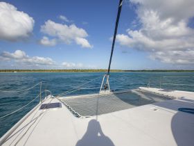 A serene view from the bow of a catamaran, showcasing the vibrant turquoise waters and lush coastline — perfect for exploring tropical destinations.