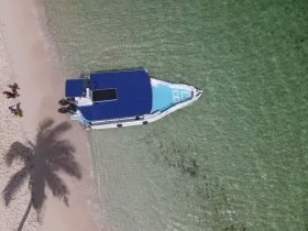 Aerial view of a boat anchored near the beach with guests enjoying the sun and sand — a perfect setting for a sandbar stop.