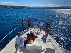 A lively group enjoys a fun day on the boat, celebrating with drinks and laughter against the stunning ocean backdrop.